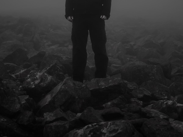Man standing among dark foggy rocks, pictured from waist down