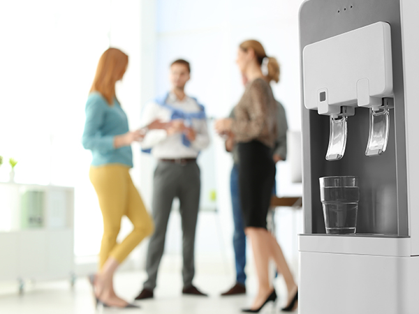 Office workers talking in background, water cooler foreground